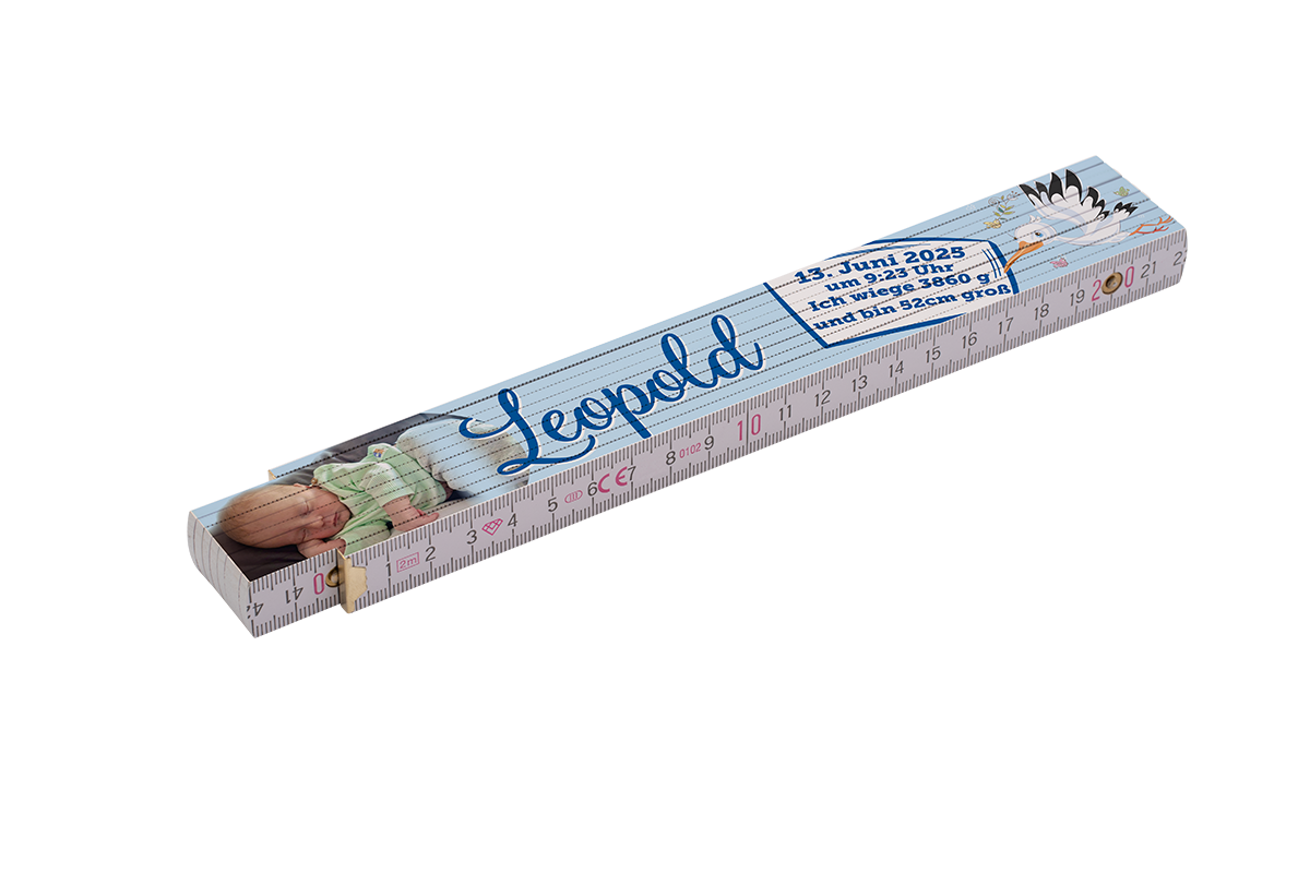 Faltmaßstab mit Babyfoto links, großem blauen Namenszug „Leopold“ in der Mitte, einer Storch-Illustration und eingedruckten Geburtsdaten (13. Juni 2025, 9:23 Uhr, 3860 g, 52 cm) sowie einer Zentimeter-Skala entlang der Kanten.