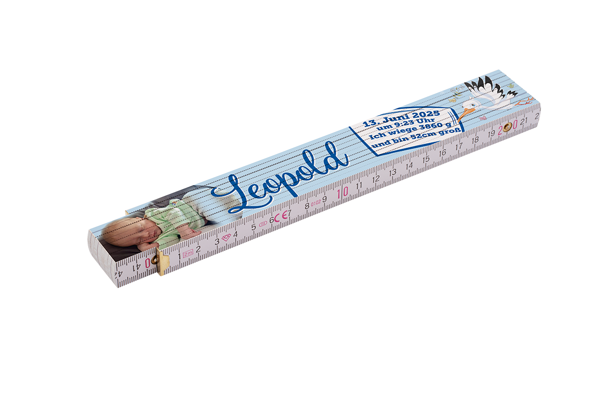 Gefalteter Holzmaßstab mit Zentimeter-Skala, bedrucktem Babyfoto, blauer, handschriftlich wirkender Namensschrift, Storch-Illustration und gedruckten Geburtsdaten (Datum, Uhrzeit, Gewicht, Größe)