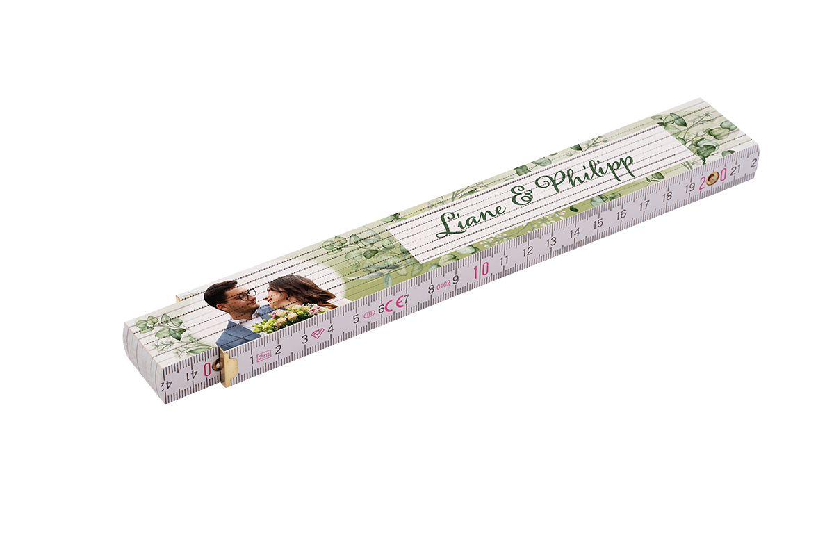 Gefalteter Holz-Zollstock mit sichtbarer Zentimeter-Skala und Messmarkierungen, dekoriert mit einem Foto eines Paares, grünen Blatt-Illustrationen und dem Schriftzug Liane & Philipp.